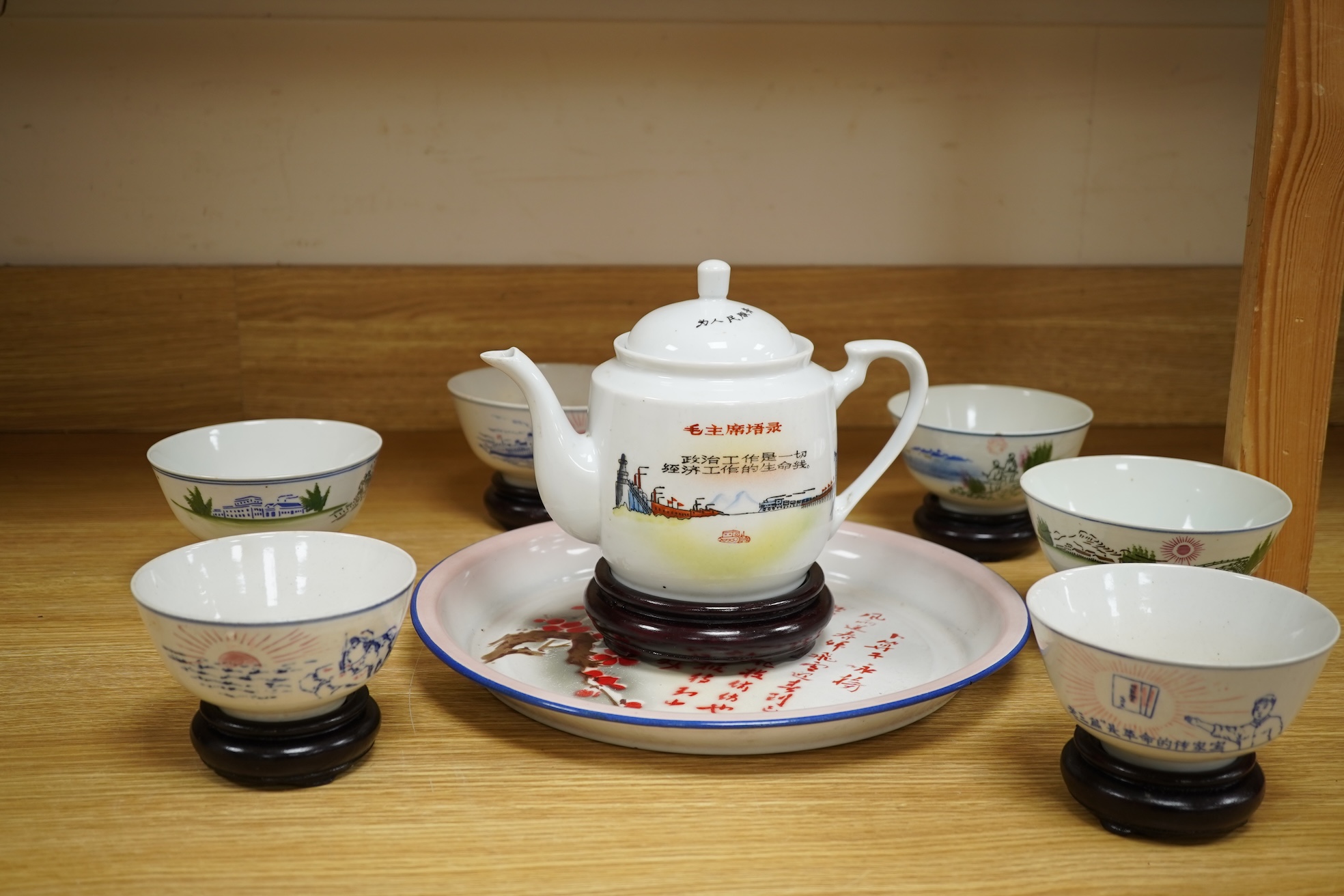 A Chinese Cultural Revolution porcelain teapot, six bowls, wood stands and an enamel tray-29.5cm diameter. (8)